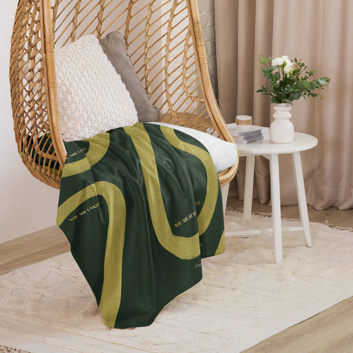 Green and gold blanket draped over a wicker chair in a cozy room with a small table and flowers.
