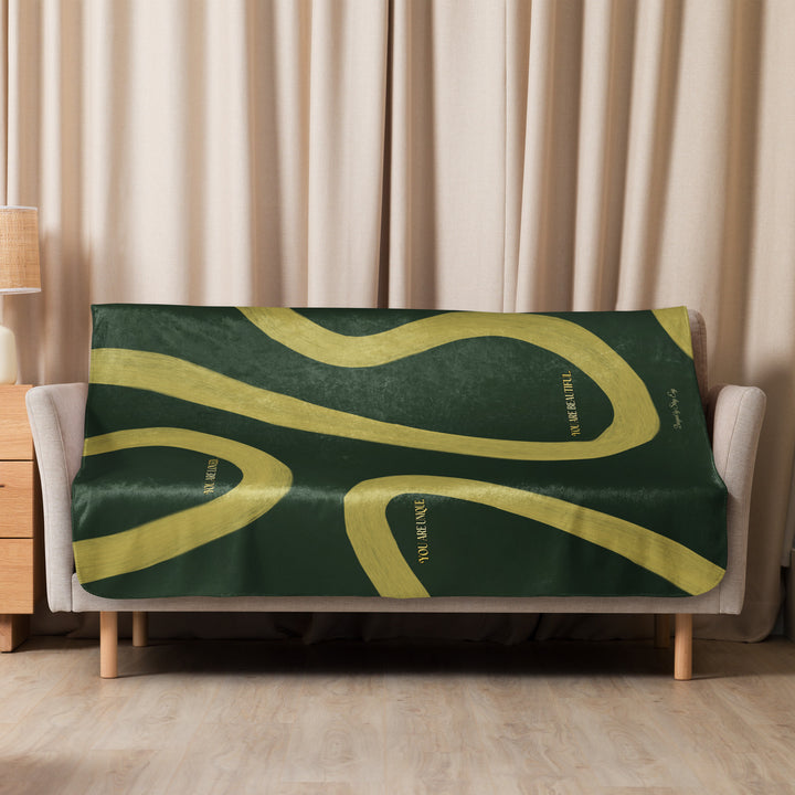 Green and yellow patterned blanket on a sofa with beige curtains in the background