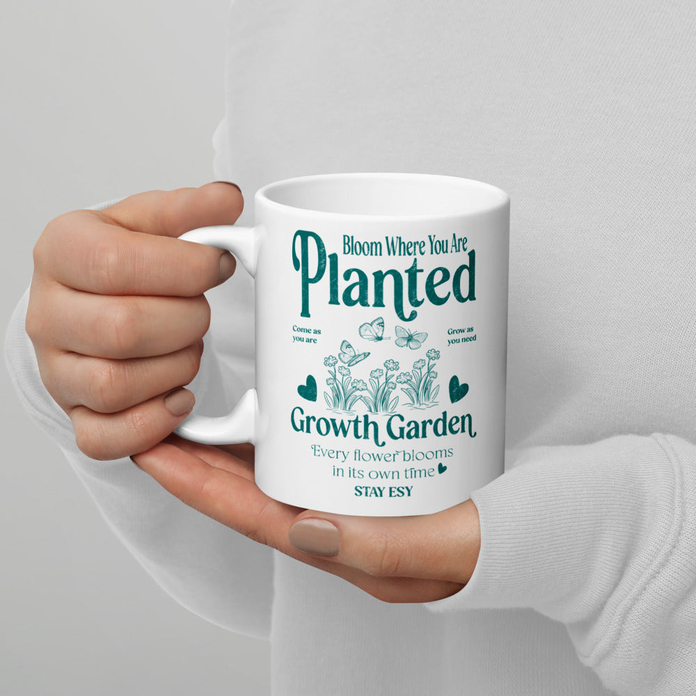 Hand holding a white mug with green text and gardening-themed design on a light gray background