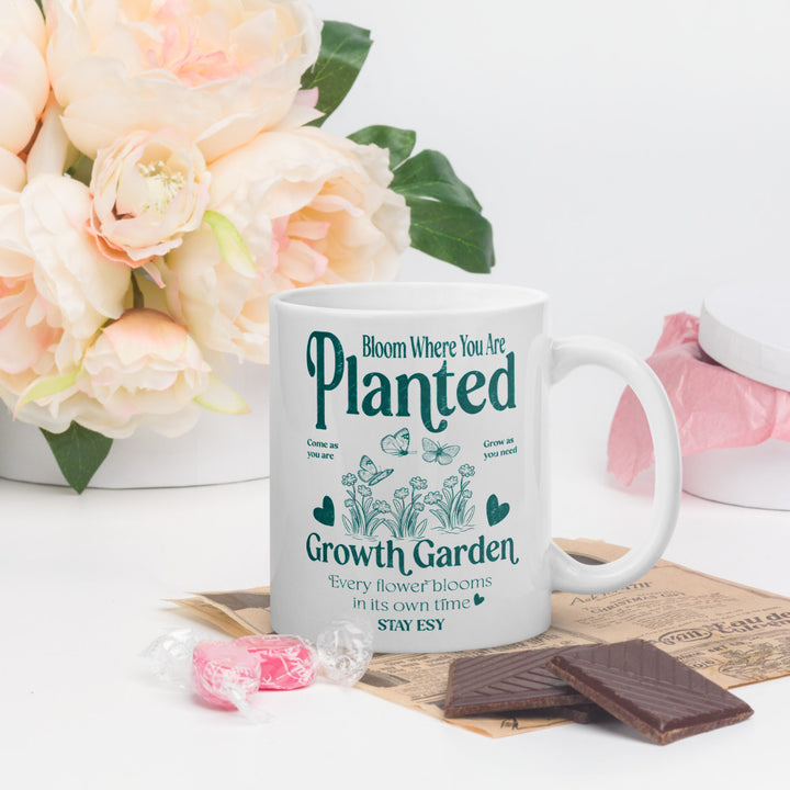 Mug with motivational quote surrounded by flowers and snacks on a light background